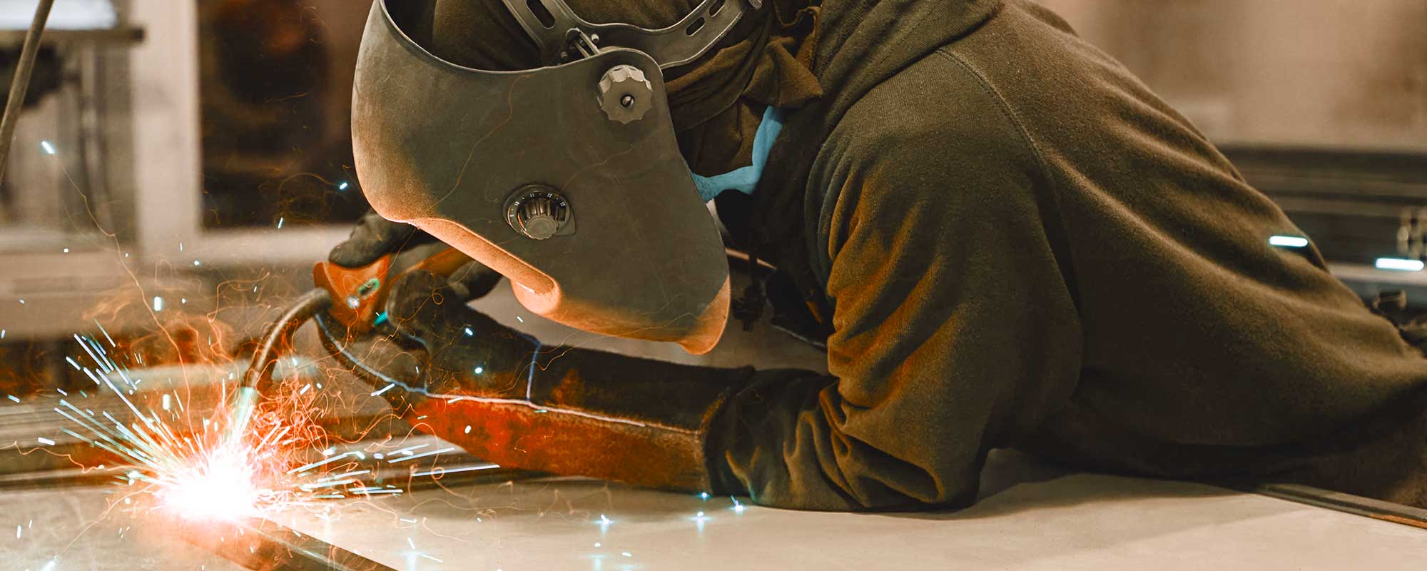 Male worker wearing helmet and gloves welding steel construction at the factory. Horizontal shot. Close up. Side view